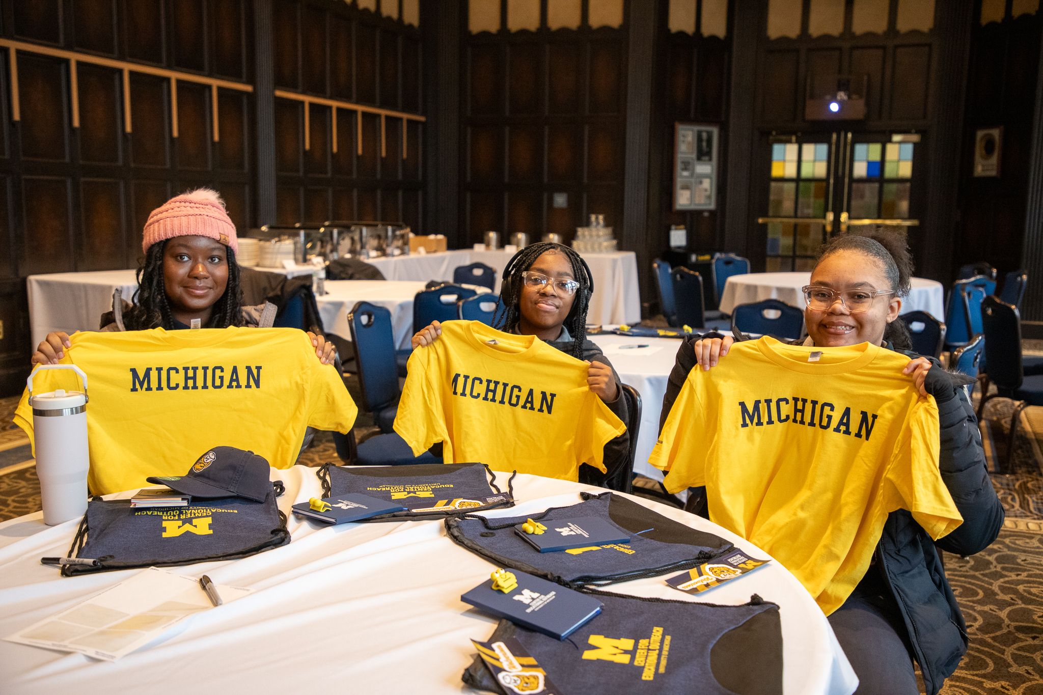 Students sitting a table holding up yellow Michigan t-shirts