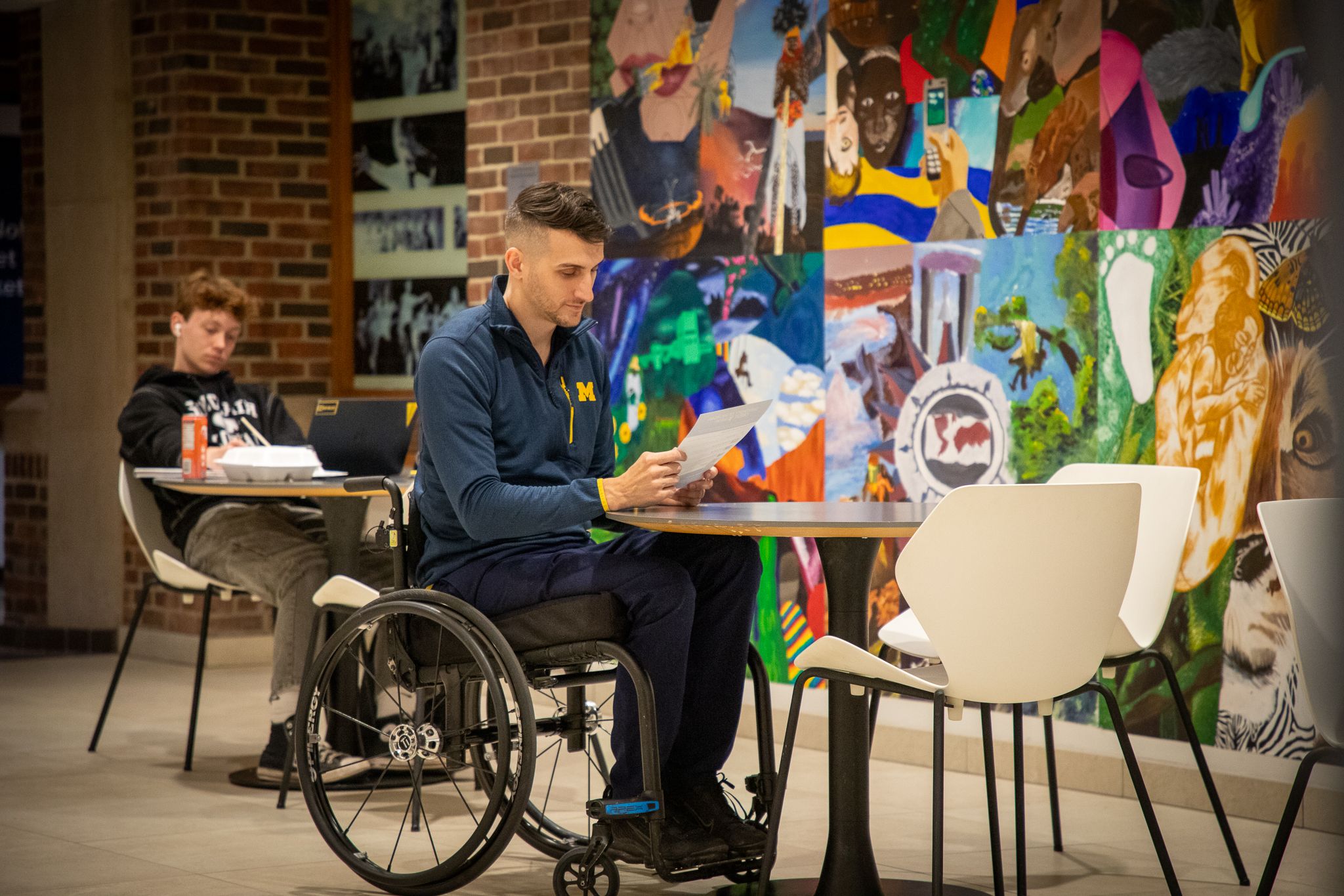 A person sitting in a wheelchair reading at a table