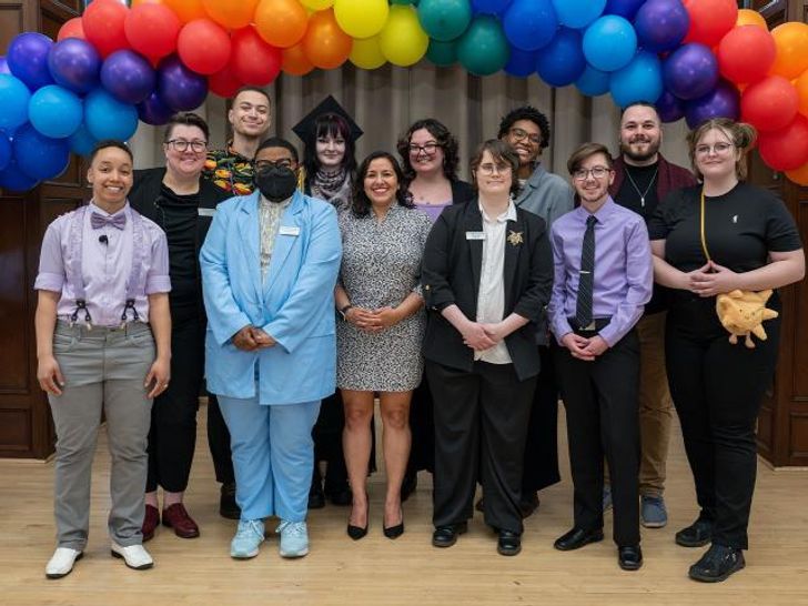 People attending the Lavender Graduation celebration under a rainbow made of balloons