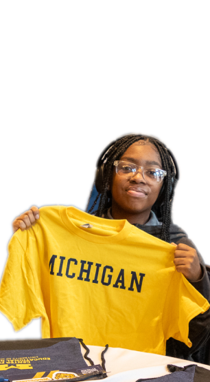 A person holding up a yellow Michigan t-shirt