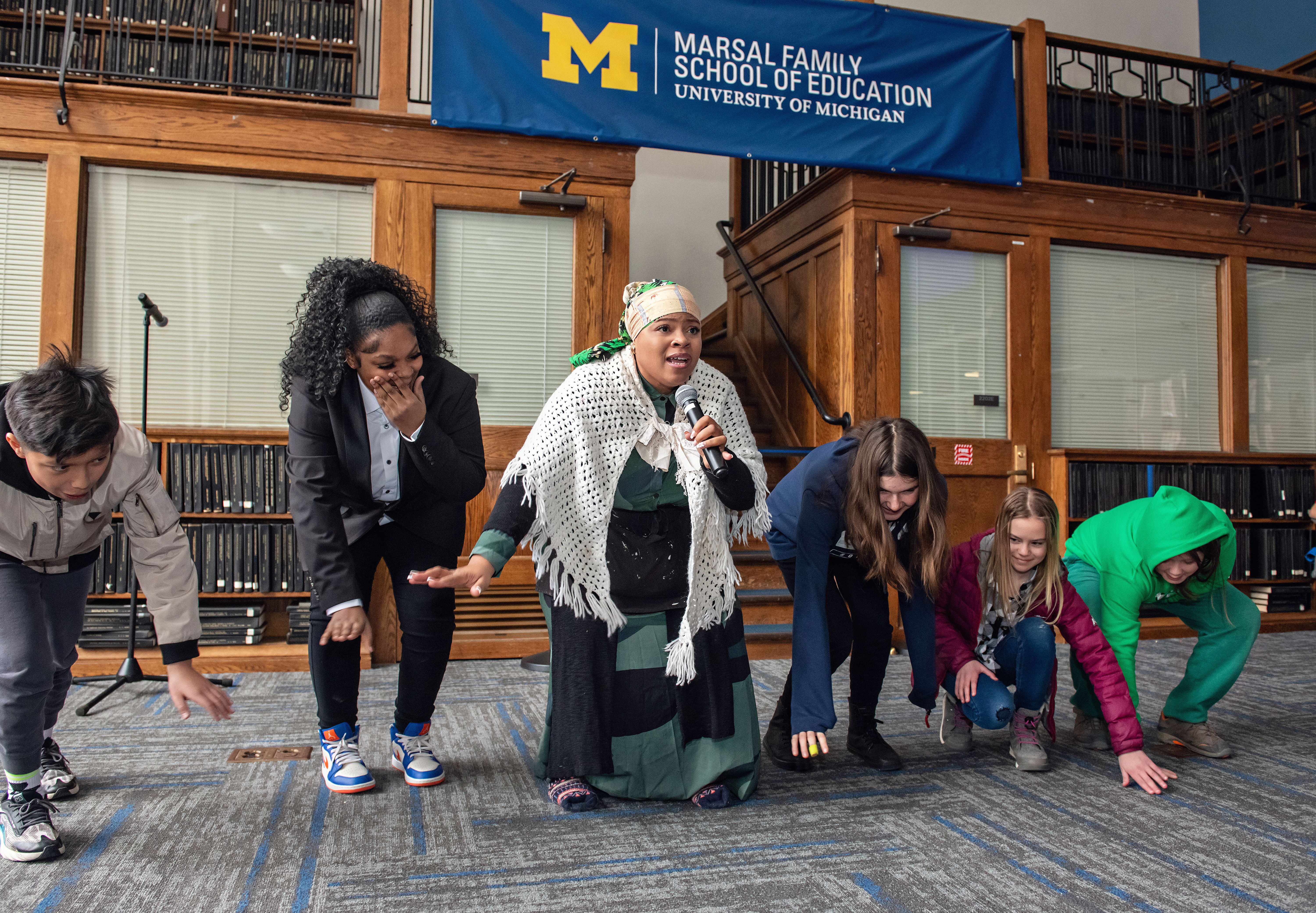 People crouching while doing an activity in front of a Marsal Family School of Education banner