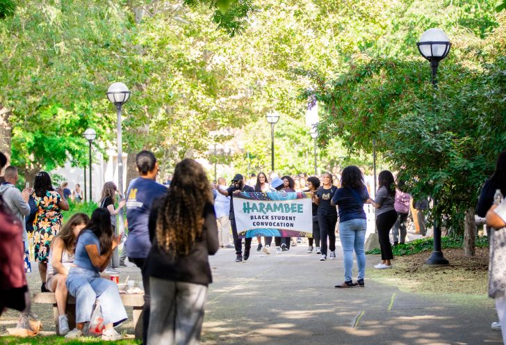 Students walking across campus carrying a Harambee Black Student Convocation banner