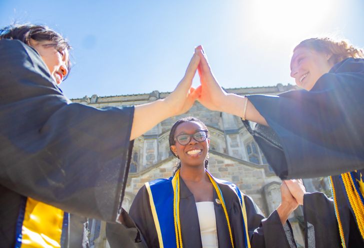 Graduates putting their hands together under a bright sun